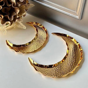 Gold crescent-shaped earrings on a white surface with decorative elements.